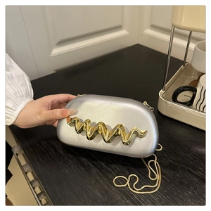Detail of silver frosted box bag with golden wave design and chain strap on table