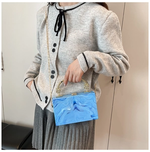 Blue marble acrylic box bag shown on model with gold metal handles and chain strap
