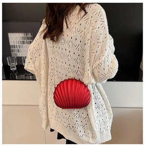 Detailed back view of a red shell-shaped evening clutch with gold chain strap on a model