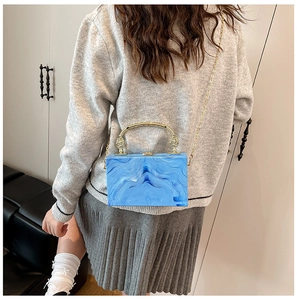 Detailed view of a blue marble acrylic box bag with golden handle on model's side