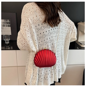 Red shell-shaped evening clutch with pleated texture and gold chain on model shoulder