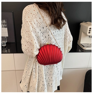 Macro detail of red shell-shaped evening clutch bag with gold chain and radial texture