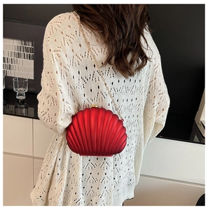 Detail of red shell-shaped acrylic evening bag with gold chain on model in white sweater