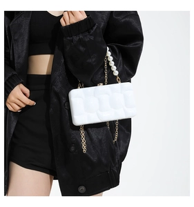 Detailed view of white acrylic clutch bag with pearl handle and gold chain on model
