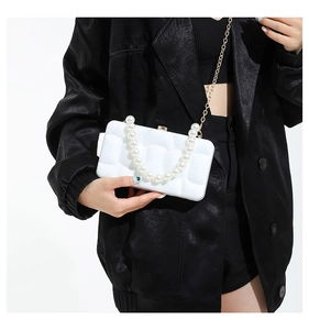 Detail of white acrylic box clutch with square texture, pearl handle, and gold chain strap
