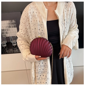 Fashionable burgundy shell evening clutch bag with gold chain strap worn by a model