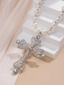 Detail of silver vintage hollow cross pendant with rhinestones and white pearls