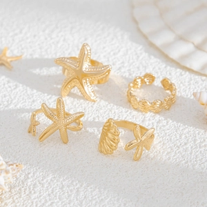 Detail of four-piece gold starfish and seashell adjustable ring set on white shell background