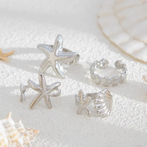 Detailed view of silver sea star and shell open rings on white sand background