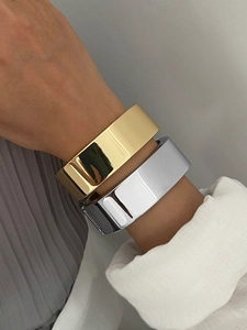 Gros plan de bracelets larges en métal poli doré et argenté sur le poignet d'un mannequin
