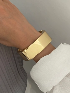 Gros plan d'un large bracelet manchette en métal doré poli porté sur le poignet