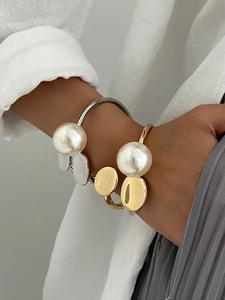 Detailed view of luxury open bracelets with oversized pearls and flat metal discs in gold and silver