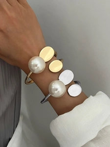 Detailed view of irregular geometric bangles with large pearls in gold and silver finish