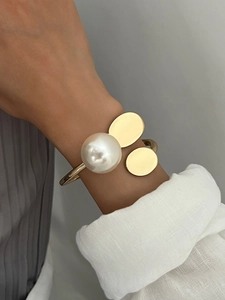 Detail of a gold open cuff bracelet with large pearl and polished metal charms