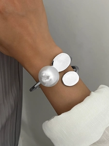 Close-up of minimalist silver cuff bracelet with large white pearl and oval metal plates