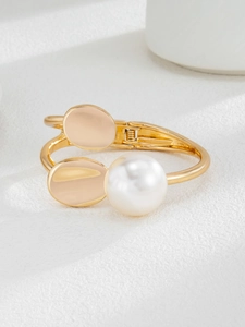 Detail of a gold hinged bracelet featuring a large white pearl and polished metal ovals
