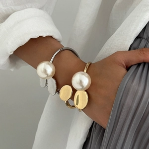 Elegant gold and silver open bangles with large pearl on a model's wrist with linen shirt