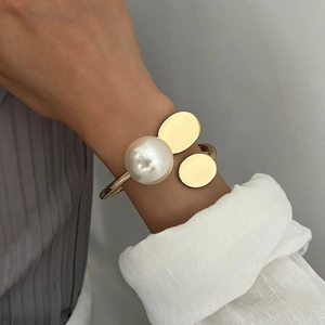 Irregular gold open bangle featuring a large pearl and oval metal discs worn on wrist