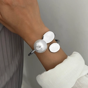 Irregular silver cuff bracelet with pearl accent and polished disks on wrist