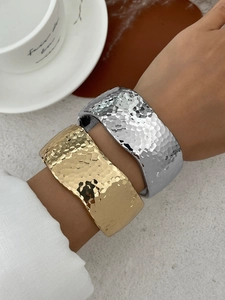 Detailed view of wide metal open bangles featuring unique hammered texture in gold and silver