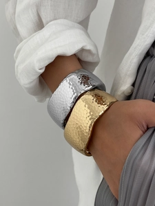 Macro detail of wide hammered alloy bangles in gold and silver showing textured finish