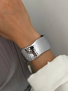 Close-up of a wide silver alloy cuff bracelet with a hammered texture and minimal design