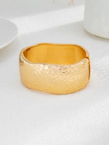 Close-up of a wide gold-plated cuff bracelet featuring a textured hammered honeycomb pattern