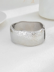 Macro shot of silver-colored wide hammered alloy cuff bracelet with irregular wavy edges