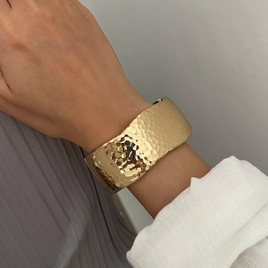 Women's wide gold open bangle with a textured hammered finish on a model's wrist