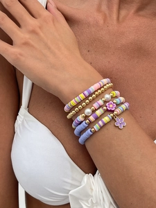 Detail von mehrlagigen Boho-Armbändern mit bunten Heishi-Perlen und goldenen Blumenanhängern
