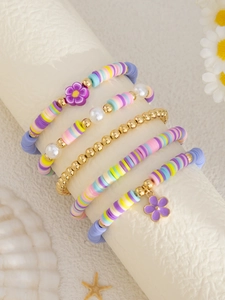 Detail von buntem Polymer-Ton-Perlenarmband-Set mit Goldperlen und Blumenanhängern