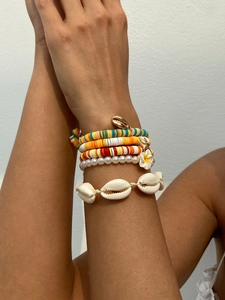 Nahaufnahme bunter Heishi-Armbänder mit goldenem Seeschnecken-Anhänger und Frangipani-Blüte