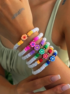 Detail von bunten Heishi-Armbändern mit Blumenanhängern und goldenen Perlen am Handgelenk