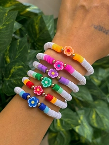 Nahaufnahme von sechs bunten Heishi-Perlenarmbändern mit Goldakzenten und Blumenanhängern