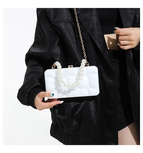Detailed view of white acrylic clutch bag with pearl handle and golden chain strap