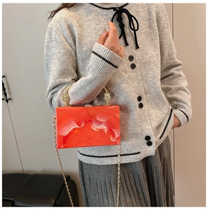 Detail of orange marble acrylic box bag with gold handle and chain on a model