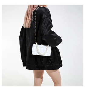 Detail of white acrylic box bag with pleated texture, pearl handle and gold chain strap