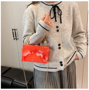 Detail of orange acrylic marble clutch bag with gold handle and chain strap on person