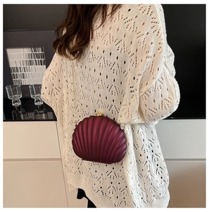Burgundy shell-shaped evening bag with gold chain strap shown on person in domestic setting