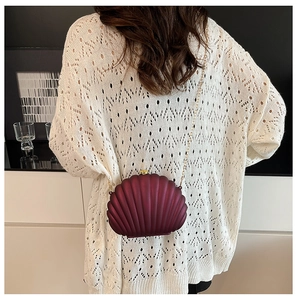 Detail view of a shell-shaped burgundy clutch with gold chain on model's shoulder
