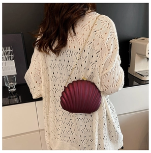 Detailed back view of a burgundy shell evening bag with a gold chain on a model