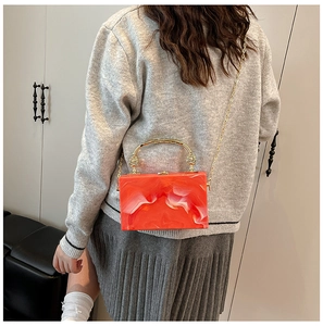 Detail of orange marble acrylic handbag with gold handle and metal chain strap