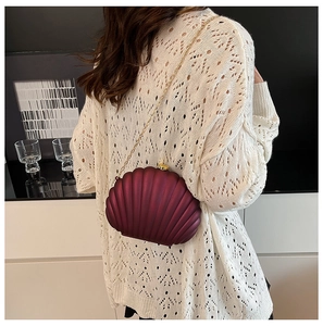 Detail of matte burgundy shell shaped clutch bag with fine gold chain on model