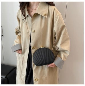 Detail view of a black shell evening bag with golden chain on a beige coat outfit