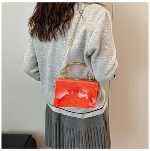 Close-up of orange marble acrylic box bag with gold metal handle and chain strap
