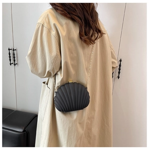 Detail of a black shell-shaped crossbody bag with relief texture and gold chain strap