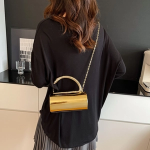 Modern gold cylindrical evening clutch bag with metal handle and chain strap shown on model