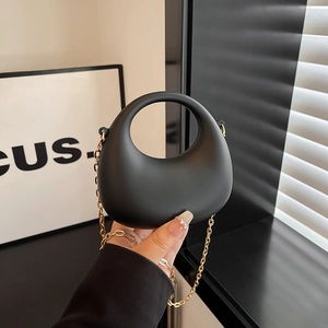 Black half-moon acrylic handbag with gold metal chain shown from a hand-held angle
