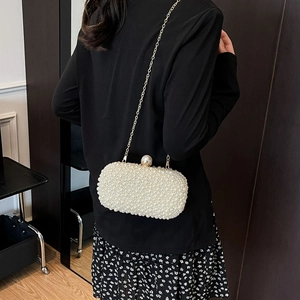 Elegant white pearl clutch bag with gold chain strap worn by a model in formal attire