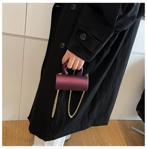 Close-up of a burgundy acrylic cylinder evening bag with gold chains and top handle